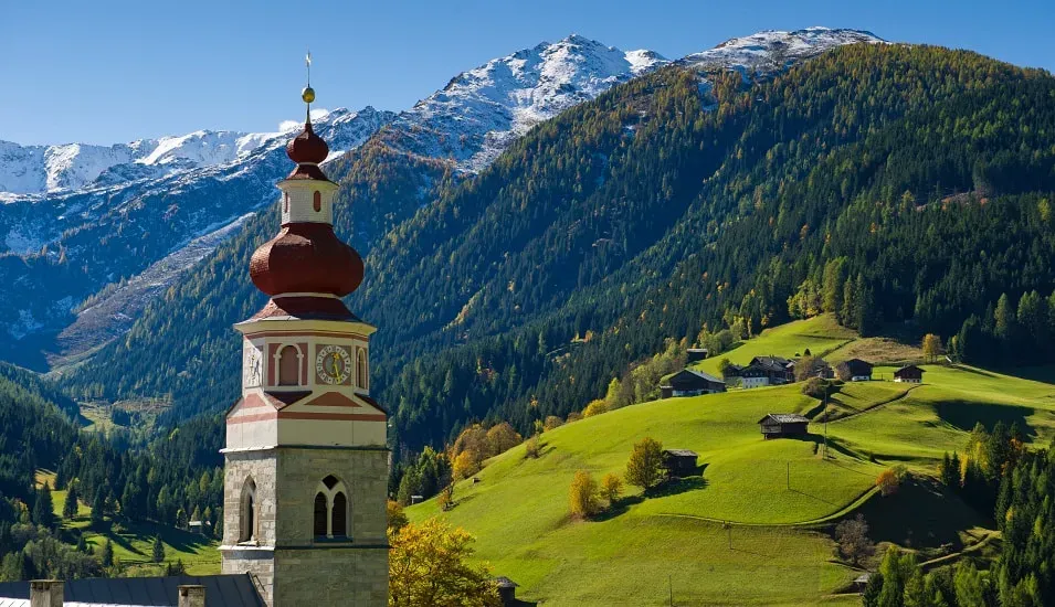 Kirchturm vor grüner Wiese und Bergpanorama